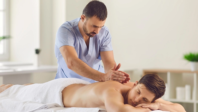 Relieving back muscle tension. Professional masseur massaging young man's back using Tapotement or chopping, tapping or hacking technique during Swedish massage therapy in spa salon or wellness center