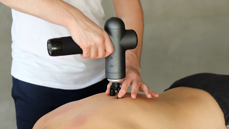 Sports percussion massage in medical room of gym. Masseur does massage exercises. Percussions therapy for regenerating massage of sport body. Concepts of rehabilitation of sports injuries.