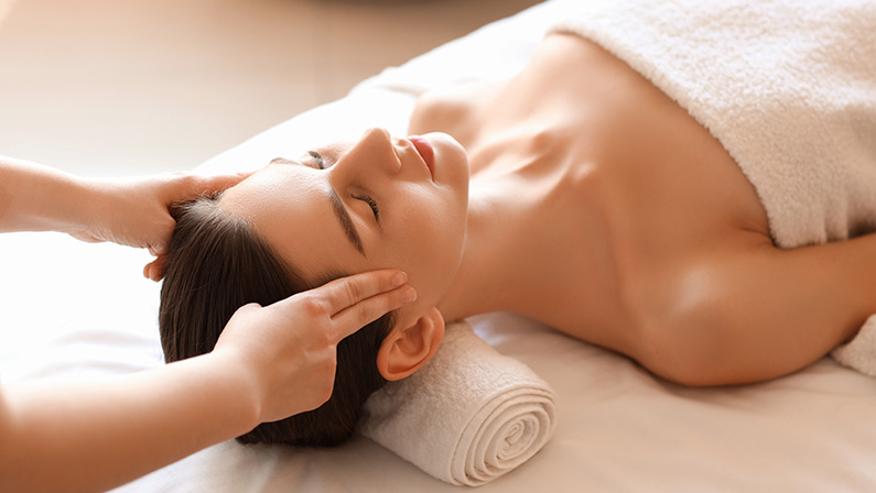 Young woman getting head massage on couch in spa salon, closeup