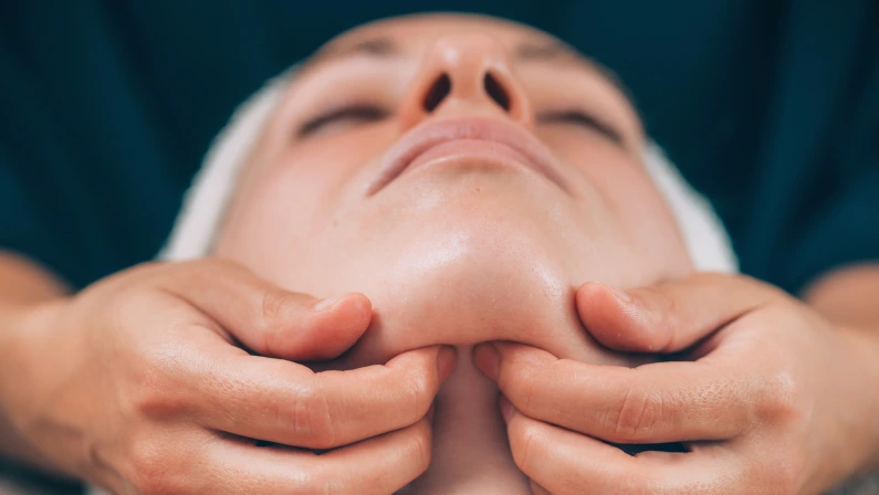 Close-up of a young woman receiving chin and jawline face lifting massage