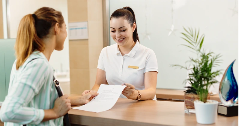 Happy massage therapist communicating with a customer at reception desk at the spa.
